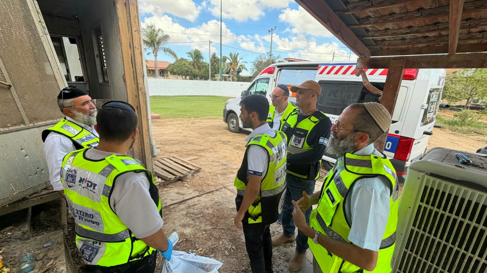 מתנדבי זק"א עומדים ליד הבית בשיחה לפני תחילת העבודה, ברקע ניידות המארגן